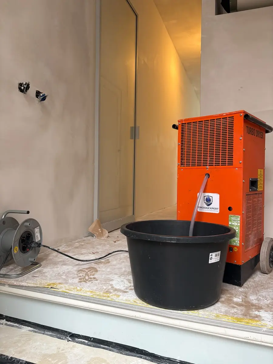 Droogapparatuur met condensafvoer en opvangemmer in een Amsterdamse kamer